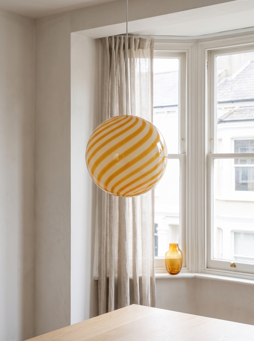 Living room pendant light in a bay window with sheer curtains – the yellow BO-HA Kaja globe.