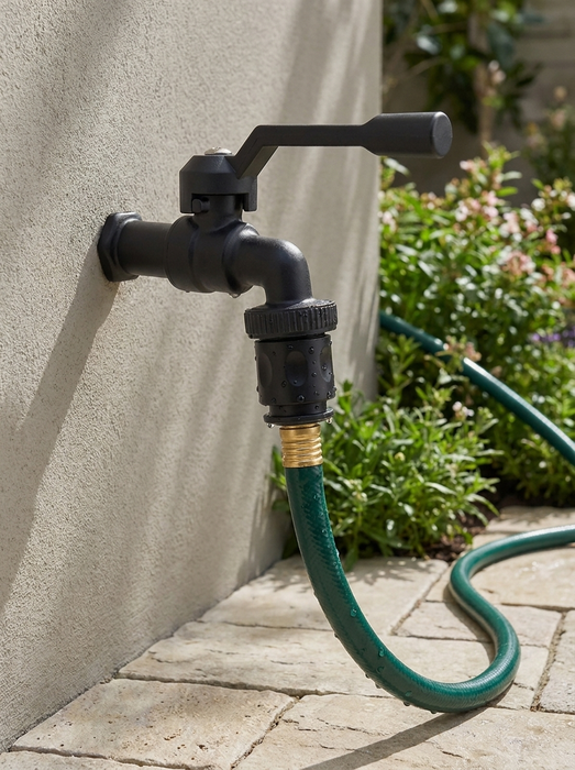 Skade – black outdoor garden faucet on a stucco wall with green garden hose connected – outdoor bibcock in garden setting